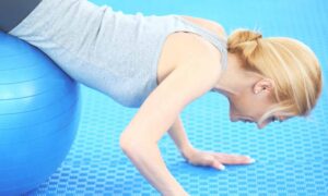 Mujer joven haciendo flexiones sobre un balón grande de color azul